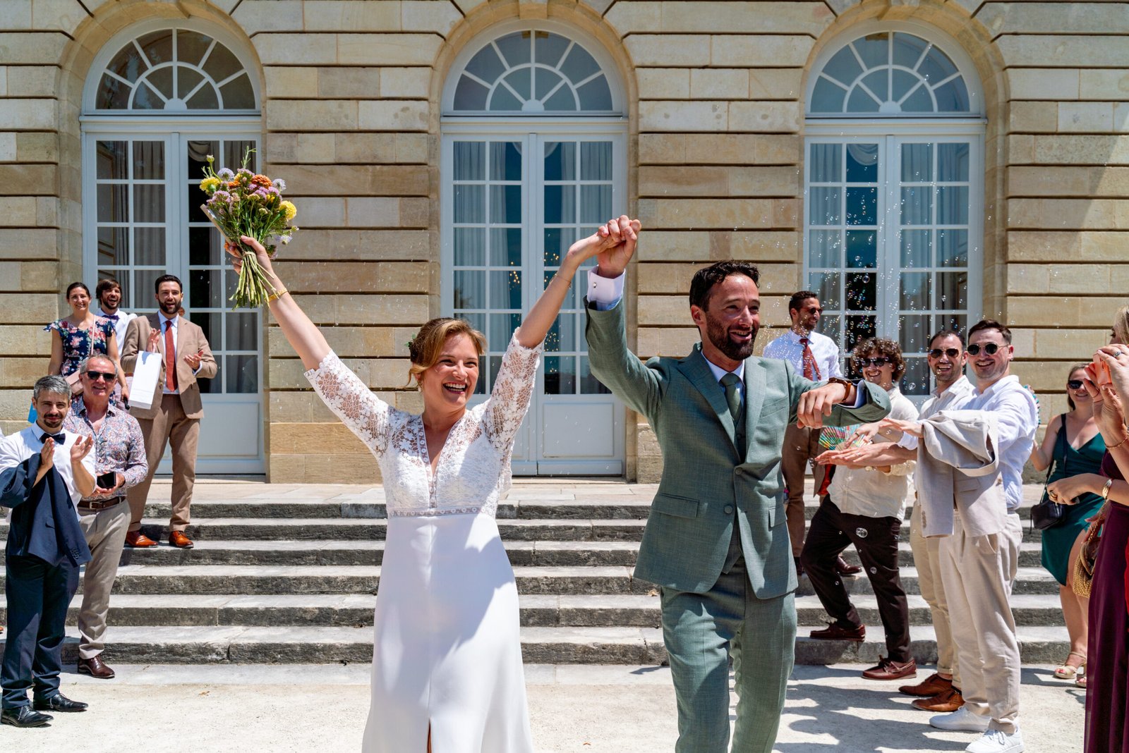 Mariés en liesse à la sortie de la cérémonie devant un bâtiment, mariage à Saint-Emilion